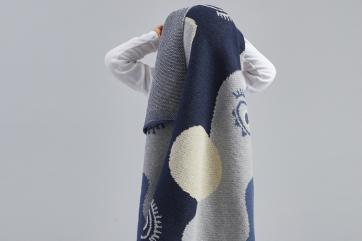 Infant holds blanket with moons and eye designs over head