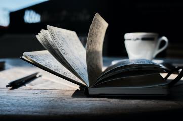 A book filled with writing sits on a table with a cup for tea 