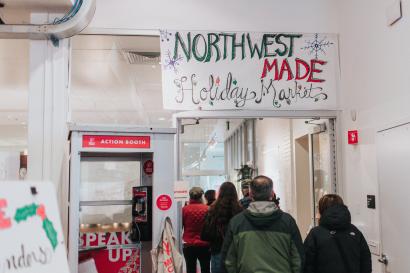 Shoppers walk under a sign titled "northwest made" at the 2019 in-person holiday market
