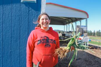 Woman stands with a leek in hand in front of shed