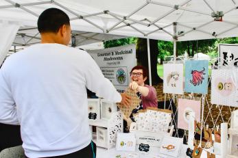 Charlene hands a product to a customer at their market booth