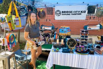 Chelsea stands in her outdoor products booth at a local market