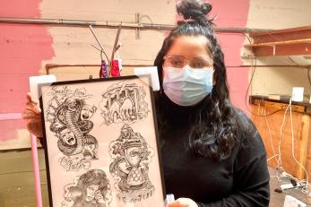 Rebecca holds a framed piece by california-based chicano tattoo artist chuco moreno in her soon-to-be lofted office above the ice queen store.