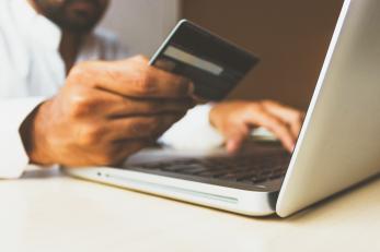 man holds credit card while on his laptop