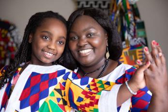 Woman sits with her daughter on her lap in african textile print clothing she designed