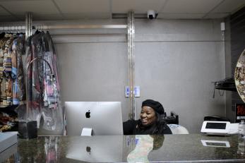 a black woman entrepreneur dressed in black sits behind her store counter with a smile