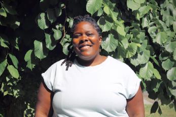 summer brown, a black femme therapist, stands in front of trees smiling