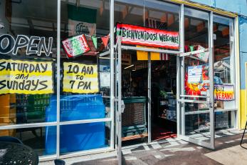 the front of a marketplace shows window designs and welcome in English and Spanish