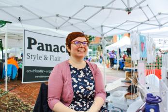 nonbinary entrepreneur smiles in their booth at a farmers market