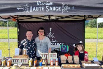 woman, man and their daughter stand a farmers market bootth