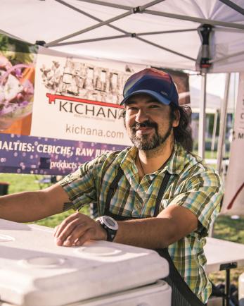 Peruvian chef stands in a farmers market booth