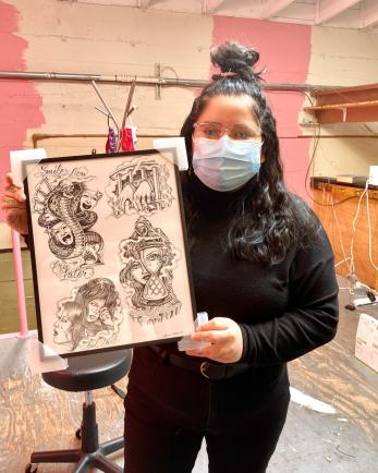 Rebecca holds a framed piece by California-based Chicano tattoo artist Chuco Moreno in her soon-to-be lofted office above the Ice Queen store.