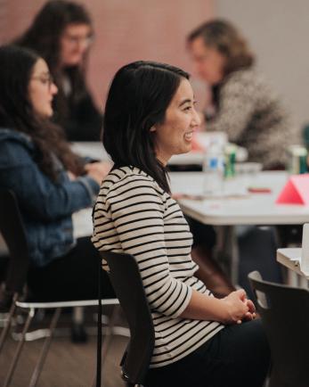 Woman sits at table in a room full of women talking during a business mentoring event