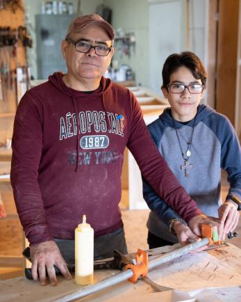 A carpenter and their son pose while working.