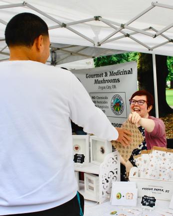 charlene hands a product to a customer at their market booth