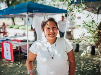 Woman standing in "farmer's market" venue in front of tent.