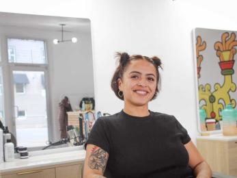 Latina woman with a bright smile sits in hair salon chair of business she owns