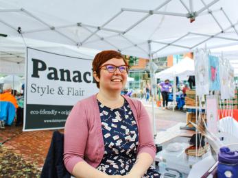 nonbinary entrepreneur smiles in their booth at a farmers market